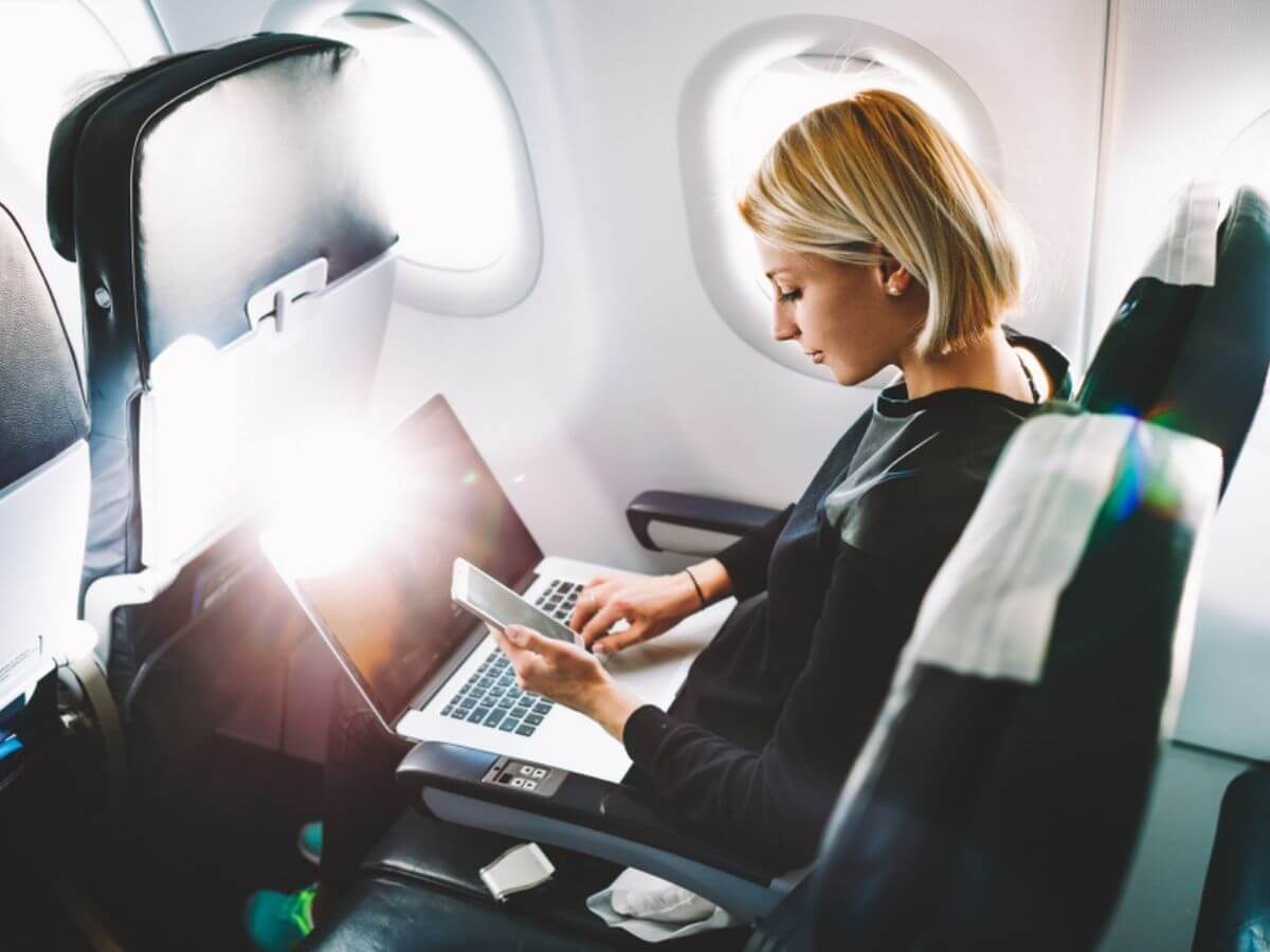 Young business woman checking phone and laptop during a plane flight