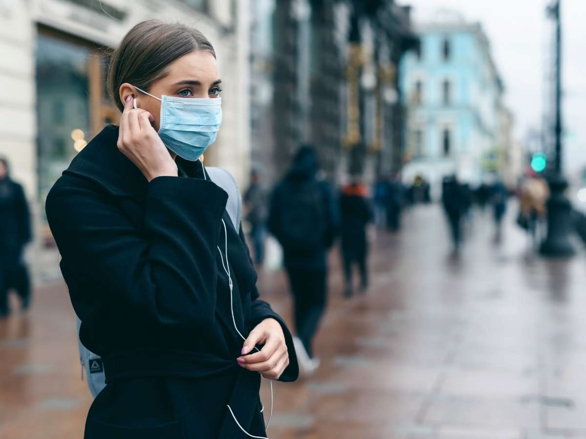 Portrait of a young woman wearing a mask in a city street.