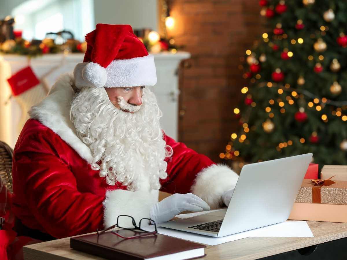 Santa with presents and a laptop sitting in front of a fireplace