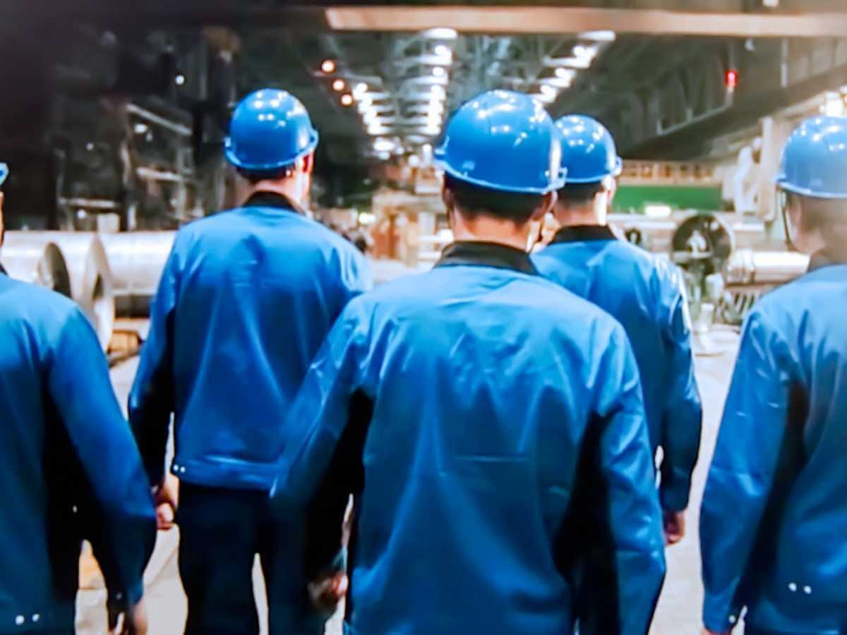A group of workers in blue shirts and hard hats walking through a large factory