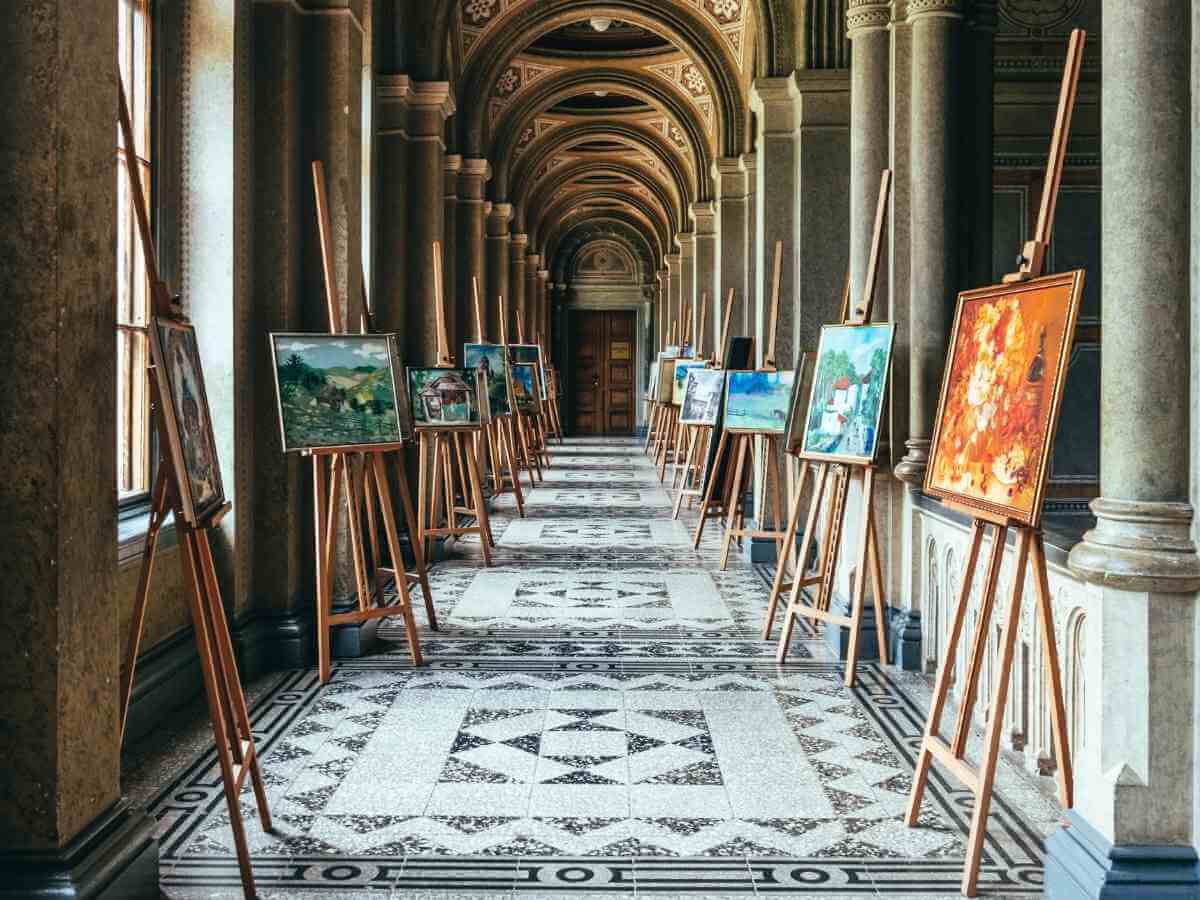Arched stone corridor in heritage building with paintings displayed on easels