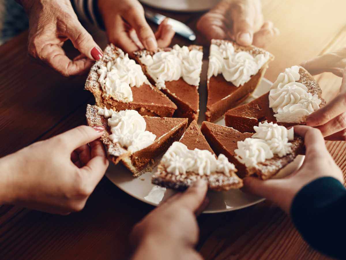 Close up of a cut up pie with family taking slices and sharing.