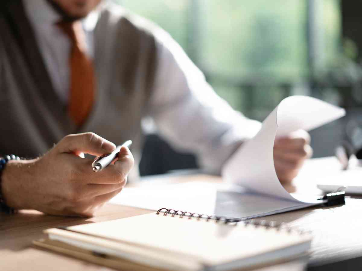 FBT audit image | Man in vest and orange tie sitting at desk looking through paperwork.