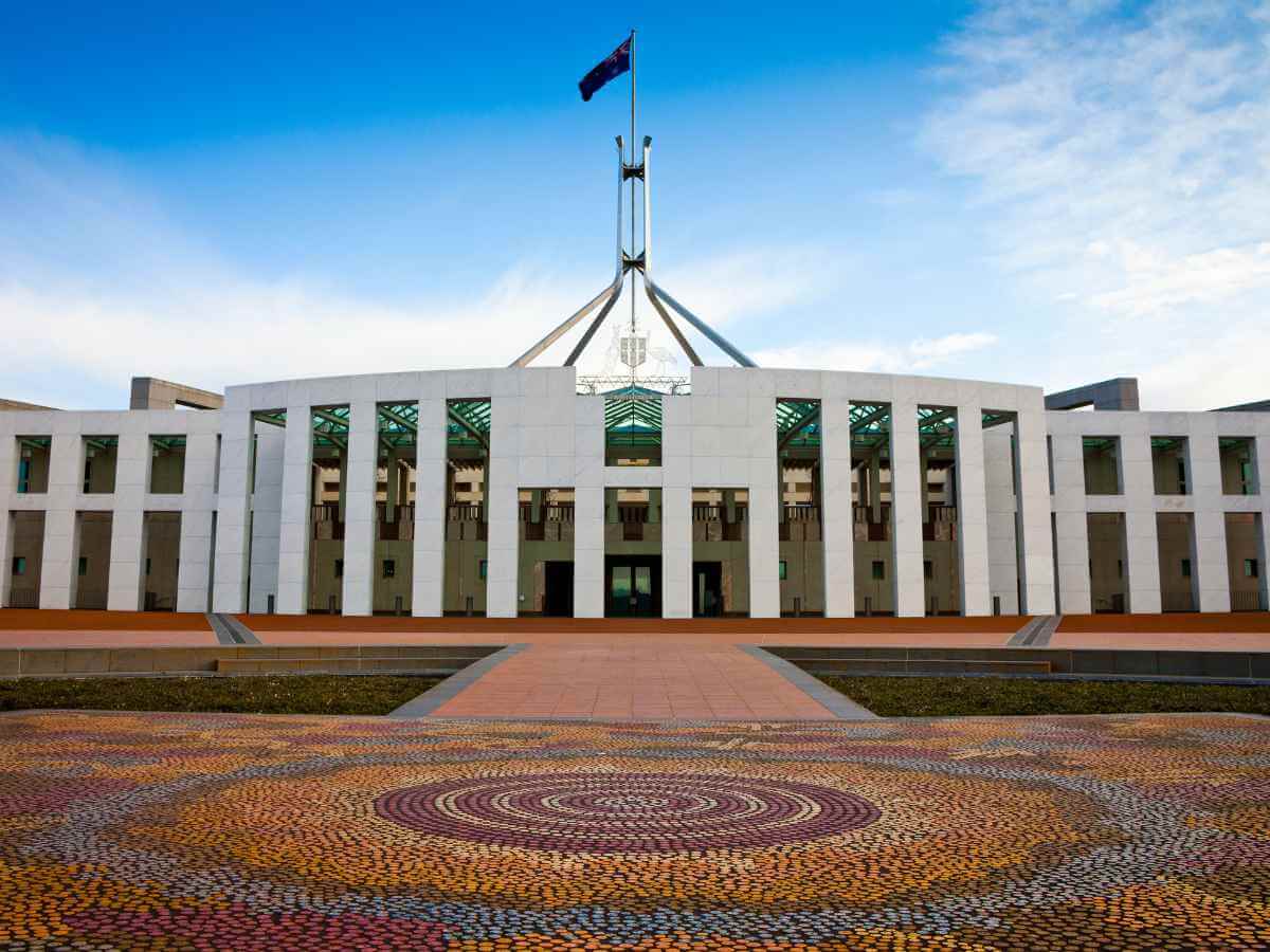 Image of the front of Parliament House in Canberra on a sunny day showing the indigenous artwork in the forecourt