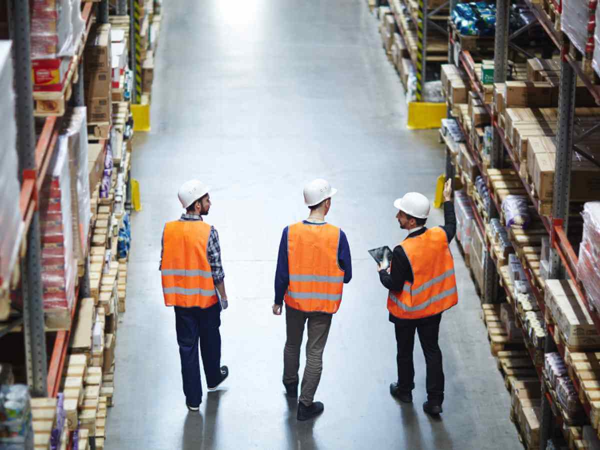 1 July 2023 wage increase | Three male workers in orange safety vests walk through a warehouse