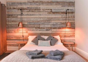 Airbnb concept image - a modern bedroom with rustic wooden headboard and white linen and pillows, copper lamp shade.