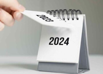 a close up black and white image of a woman's hand turning over a calendar sheet showing the year change from 2023 to 2024