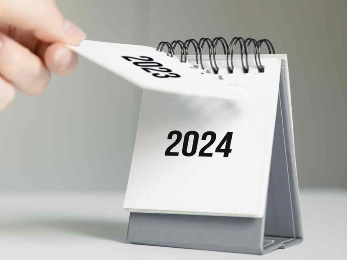 a close up black and white image of a woman's hand turning over a calendar sheet showing the year change from 2023 to 2024