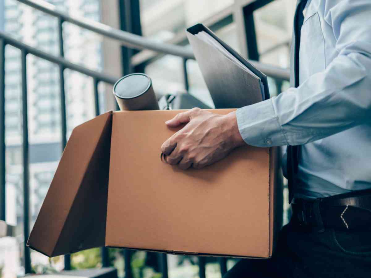 Leaving a job concept image – A male professional wearing a blue business shirt and tie is holding a cardboard box containing files, a briefcase and a drawing tube.
