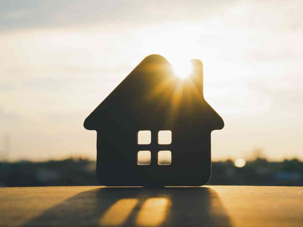 Bank of Mum and Dad concept | Close up of the sun shining on a cut out house with blurred suburban background